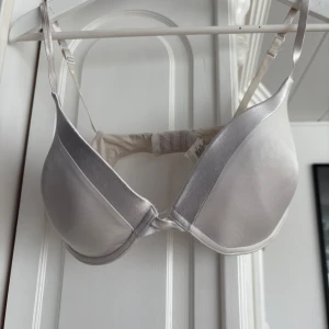Vit satin-bh 80D - Säljer en stilren vit bh i satin med släta kupor och justerbara axelband. Bh:n har en enkel och elegant design som passar perfekt under ljusa toppar. Kuporna är vadderade för extra stöd och komfort. Använd 