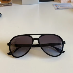 Svarta solglasögon från Ray-Ban - Snygga svarta solglasögon från Ray-Ban i klassisk pilotmodell. De har en svart ram och mörka glas. Perfekta för en stilren look. Kommer med ett brunt fodral och putsduk. Nypris 1100kr mitt pris 699kr