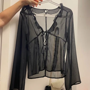 Mesh blus  - Säljer en elegant svart transparent blus med långa ärmar och knytning framtill. Perfekt för en stilfull look. Passar bra till både jeans och kjol.