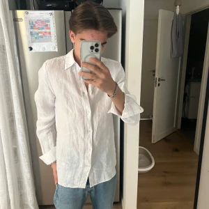 Vit linneskjorta från J.Lindeberg - Säljer en stilren vit skjorta i linne från J.Lindeberg. Skjortan har klassisk krage, knäppning framtill och långa ärmar. Perfekt för en fräsch och avslappnad look. Passar dig som gillar en normal passform och vill ha något svalt och luftigt.