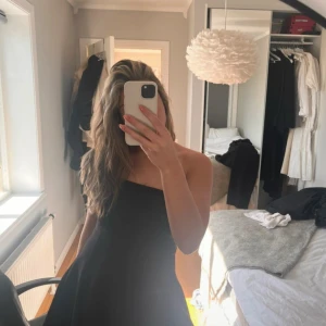 Svart axelbandslös klänning från Zara - Säljer en svart axelbandslös klänning . Klänningen har en utsvängd kjol och en enkel, stilren design som ger en snygg siluett. Perfekt för dig som vill ha en klassisk och tidlös look. Inbyggda shorts