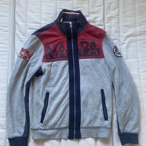 Grå och vinröd jacka från Napapijri - Säljer en grå jacka från Napapijri med vinröda och mörkblå detaljer. 