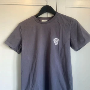 Grå t-shirt från Suspicious Antwerp - Snygg grå t-shirt från Suspicious Antwerp med ett litet tryck på bröstet. Tillverkad i 100% ekologisk bomull för en skön och hållbar känsla. Perfekt för en avslappnad stil.