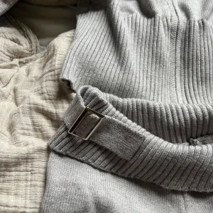 Grå ribbstickat sett - Säljer mitt ribbstickade sett med snyggt bälte i midjan och bootcut-modell. Byxorna och tröjan är stickade och har en mjuk, bekväm känsla. Perfekta för dig som gillar en trendig och avslappnad stil. 