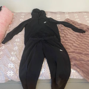 Svart hoodie och byxa från Nike - Säljer en klassisk svart hoodie och byxa från Nike med justerbar huva och känguruficka. Perfekt för en avslappnad stil. Dom har en liten Nike-logga på bröstet och benet. Passar bra till både träning och vardag. Båda i storlek s, dom kan säljas separat 
