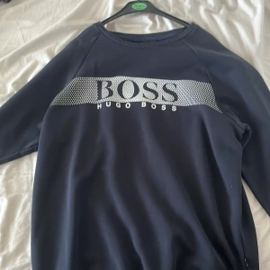 Svart tröja från Hugo Boss - Snygg svart tröja från Hugo Boss med ett stort BOSS-tryck i vitt över bröstet. Tröjan har långa ärmar och en klassisk rund halsringning. Perfekt för en stilren look.