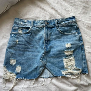 Blå jeanskjol med slitningar - Blå jeanskjol med slitningar och fransiga kanter. 