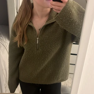 Olivgrön stickad tröja med dragkedja - Mysig olivgrön stickad tröja med halv dragkedja framtill och hög krage. Tröjan har lång ärm och en relaxed passform, perfekt för kyliga dagar. Snygg ribbad struktur. Tröjan är från hm. Det som är trist är att den är noppig. Annars väldigt varm fin tröja!🩷