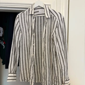 Randig linneskjorta  - Snygg och luftig skjorta i linne från Massimo Dutti. Skjortan är vit med svarta ränder och har långa ärmar samt knappar framtill. Perfekt för en stilren och avslappnad look. Storlek S, perfekt till sommaren nu och passar till alla tillfällen