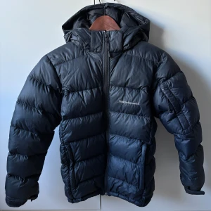 Peak Performance Frost Down Jacket Junior - Jag säljer min Peak Performance Frost Down Jacket i juniorstorlek. Ord. pris: ca 2 500kr. Mitt pris: 1 000kr. Det är en supervarm, lätt och slitstark dunjacka – perfekt för kalla vinterdagar, både till vardags och i skidbacken. Det finns ett litet märke på baksidan längst ner (kolla sista bilden) men det är inget man tänker på.