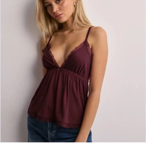 Vinröd linne med spetsdetaljer - Snygg vinröd linne med spetsdetaljer och smala axelband. Perfekt för en stilren look. Den har en djup v-ringning och en lös passform som ger en avslappnad känsla.