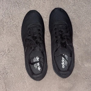 Svarta L.A. TRAINER storlek 42 helt nya  - Snygga svarta sneakers från Adidas med texten 'LA Trainer' på sidan. Skorna har en stilren design med snörning och en mönstrad sula för bra grepp. Perfekta för både vardag och träning. 