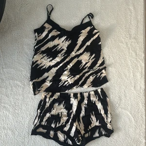 Svart och beige set med linnetopp och shorts - Snyggt set med svart och beige mönster. Linnetoppen har smala axelband och matchande shorts med elastisk midja. Perfekt för en avslappnad stil.