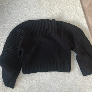 Svart ribbad tröja - Säljer en stilren svart ribbad tröja med långa ärmar. Perfekt för en trendig look. Tröjan har en croppad passform och är tillverkad i ett mjukt material.