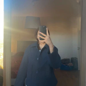 Mörkblå kappa  - Snygg mörkblå ulljacka med klassisk krage och stora knappar framtill. Jackan har två praktiska fickor och långa ärmar. Perfekt för kyligare dagar.