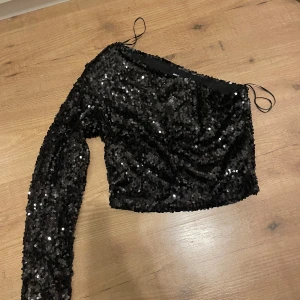 Svart paljett topp från Sinsay - Säljer en svart glittrig paljett topp från Sinsay. Toppen är oneshoulder med en lång ärm. Perfekt för dig som vill sticka ut med lite extra glitter✨ ‼️OBS Aldrig använt‼️