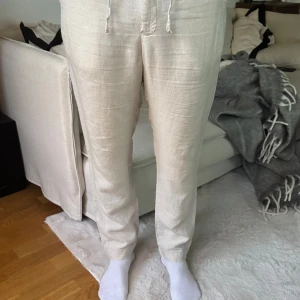 Beige linnebyxor med snörning - Snygga beige linnebyxor med snörning i midjan. Perfekta för en avslappnad stil, med en bekväm passform och praktiska fickor. Byxorna har en naturlig look och är idealiska för varmare väder.