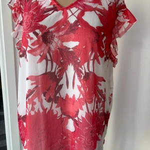 Röd och vit blommig blus från Saint Tropez - Säljer en luftig blus från Saint Tropez i storlek XL. Blusen har ett rött och vitt blommigt mönster, v-ringning och volangdetaljer vid ärmarna. Perfekt för dig som gillar färg och mönster! Använd men bra skick 
