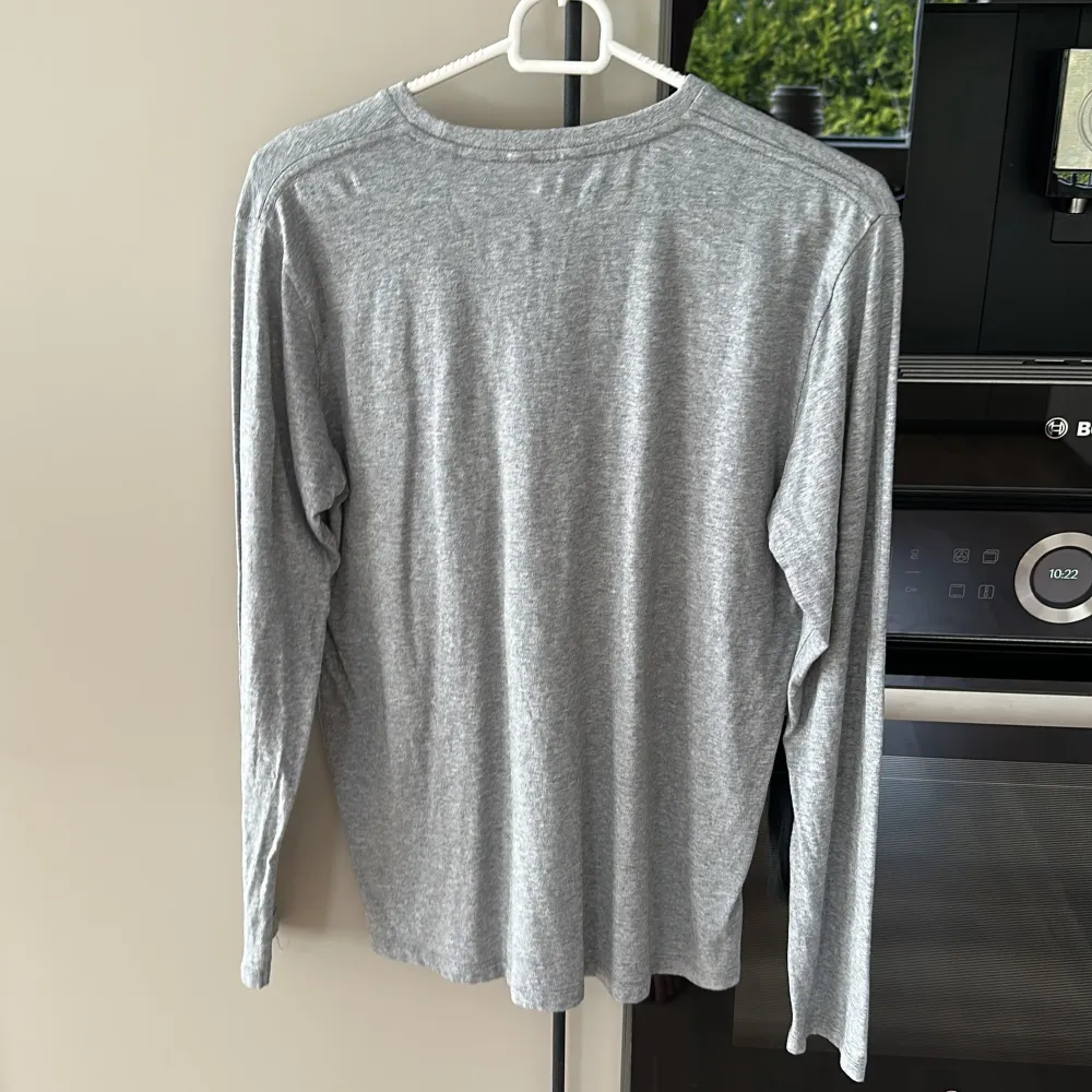 Säljer en stilren grå långärmad tröja från GANT. Tröjan har rund halsringning och en liten broderad logga på bröstet. Perfekt för en enkel och klassisk look.. Neuletakit & Villapaidat.