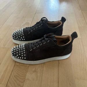 Mörk grå sneakers med nitar från Christian Louboutin - Säljer min brorsas snygga mörk grå sneakers från Christian Louboutin som han växt ur. Skorna är i bra skick men har tecken på användning. En metall ring saknas se sista bilden. Hör av er om ni har några frågor! Inga nitar saknas. En påse med nitar medföljer.