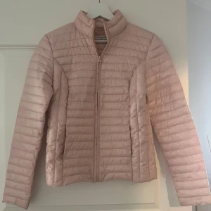 Ljusrosa pufferjacka från Jacqueline de Yong - Säljer en ljusrosa pufferjacka från Jacqueline de Yong i storlek XS. Jackan har dragkedja framtill, hög krage och quiltad design. Perfekt för kyliga dagar och enkel att matcha med olika outfits.