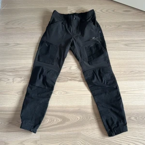 Svarta cargopants från 2117 - Snygga svarta vildmarks byxor praktiska fickor. Byxorna har en elastisk midja och justerbara benslut för optimal passform. Perfekta för en avslappnad stil eller utomhusaktiviteter.