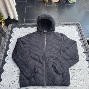 Svart quiltad jacka med huva EA7 - Säljer en svart quiltad jacka med huva och dragkedja framtill. Jackan har en stilren design och är perfekt för kyligare dagar. Den är långärmad och har en bekväm passform.