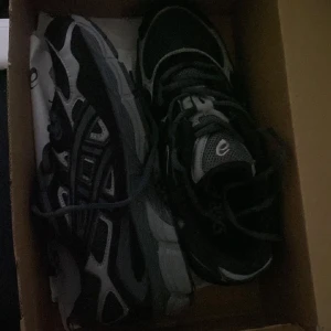  Asicss gel nyc  - Snygga assics i svart och grätt med coola detaljer och meshpaneler för extra andningsförmäga. Skorna har snörning och en robust sula som ger bra grepp. Perfekta for dig som gillar sportig stil och vill ha bekväma skor till vardagen.