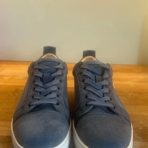 Blå mockasneakers från Louboutin - Snygga sneakers från Louboutin i blå mocka med vita sulor och klassisk snörning. Skorna har en stilren design med rund tå och diskreta detaljer, samt mjukt beige foder för extra komfort. Perfekta för dig som gillar exklusiva och trendiga sneakers. Säljer dom pga liten användning för dom, skorna har användt 2 gånger med inge syn an användning förutom på undersidan där dom bara är lite smutsiga. Vid frågor eller bud är det bara att skriva, kan gå ner i pris vid enkel och snabbt betalande!
