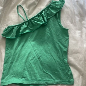 Grön oneshoulder topp från ONLY - Snygg grön topp från ONLY med en liten volang. Köpt från sellpy aldrig använt.