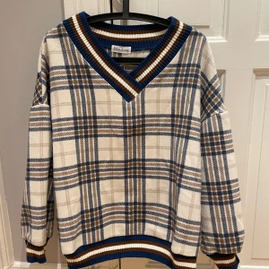 Rutig v-ringad tröja från KSparame - Säljer en oversized rutig tröja från KSparame med v-ringad hals och ribbade muddar i blått, brunt och vitt. Tröjan har långärmade ärmar och ett klassiskt rutmönster i beige, blått och brunt. Perfekt för dig som gillar retrovibbar och chill stil.