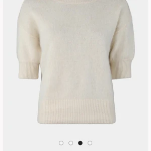 Krämvit stickad tröja med kort ärm - Supermjuk krämvit stickad tröja med korta ärmar och breda ribbade muddar. Enkel och clean design som är lätt att styla till olika looks. Perfekt för lager-på-lager under höst och vår.