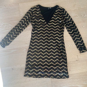 Svart och guld paljettklänning H&M - Säljer en svart och guld kortklänning från H&M Divided med långärmad design och v-ringning. Klänningen har ett glittrigt sicksackmönster av paljetter som ger en riktigt festlig vibe. Mottagaren står för frakten💕