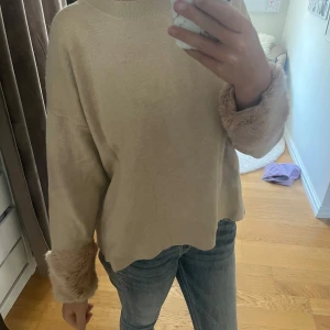 Beige tröja med fluffiga ärmar - Jag säljer en tröja från Holly&Whyte med ”lurviga” ärmar ner vid händerna som är en fin detalj. Materialet är ”hårdare” än vanligt stickat och fallet fint. Superfin och bekväm! Storlek L men passar mig perfekt som brukar ha S! 