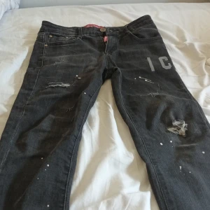 Svarta jeans med slitningar och tryck - Säljer ett par svarta jeans från Desigual med coola slitningar, vita färgstänk och tryckt text på ena benet. Jeansen har fem fickor, normal passform och är gjorda i bomull med en skön jeanskänsla. Perfekta för dig som gillar en edgy streetstil.