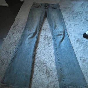 Levis bootcut jeans ljusblå lågmidjade - Ljusblå Levis jeans med bootcut passform och låg midja. Klassisk femficksmodell med snygga detaljer på bakfickorna och lätt slitning framtill. Perfekta för dig som gillar en retro vibe och vill ha ett par jeans som sitter snyggt över höften. Måtten är 34/36 jeansen är köpta secondhand i Paris lite slitna 