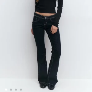 Mörkblå bootcut jeans med kontrastsömmar - Snygga mörkblå jeans med bootcut passform och vita kontrastsömmar. Låg midja och klassisk femficksdesign. Jeansen har en markerad utsvängning nedtill och är tillverkade i kraftigt denimtyg. Perfekta för dig som gillar retrovibbar och markerad siluett.