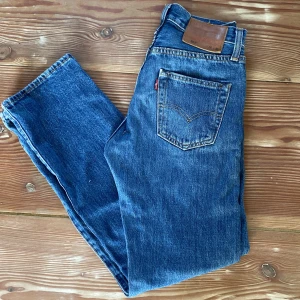 Levi's 501 jeans - Klassiska blå Levi's 501 jeans storlek w26 l30 med raka ben och knappgylf. Byxorna har fem fickor och tydliga sömmar, samt den ikoniska läderpatchen bak i midjan. Perfekta för en tidlös och avslappnad stil.