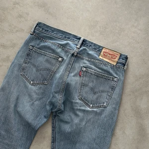 Levi's 501  - Klassiska Levi's 501 jeans i ljusblå tvätt med raka ben och normal passform. Jeansen har fem fickor, knappgylf och den ikoniska läderpatchen bak i midjan. Tillverkade i slitstarkt bomullsjeans, perfekt för en avslappnad och tidlös look.