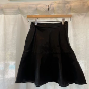 Svart skinnkjol från J.Lindeberg - Snygg svart kjol från J.Lindeberg i skinnimitation. Kjolen har en lätt utsvängd form och sitter snyggt i midjan ❤️‍🔥