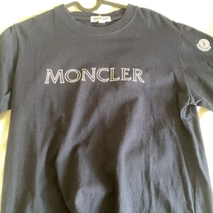 Svart Moncler t-shirt med logga - Svart t-shirt från Moncler i bomull med stor vit Moncler-logga på bröstet och klassisk patch på ärmen. Jätte bra skick! Pris kan diskuteras!!