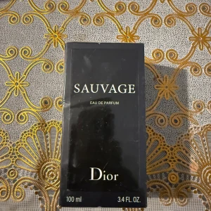 Dior Sauvage Eau de Parfum 100ml - Dior Sauvage Eau de Parfum i en elegant svart förpackning med guldtext. Flaskan rymmer 100 ml och doften är känd för sin fräscha, maskulina och kryddiga karaktär. Perfekt för dig som vill ha en ikonisk och modern parfym.