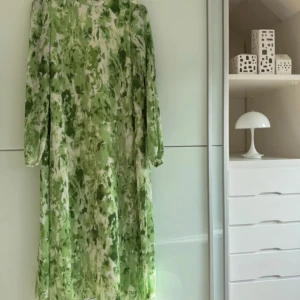 Grönvit långklänning från Y.A.S - Superfin långklänning från Y.A.S i grönt och vitt med blommigt mönster. Klänningen har plisserat tyg, hög krage med volang och trekvartsärmar. Tillverkad i mjuk polyester och perfekt för vår och sommar.