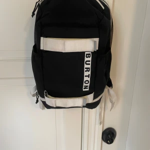 Burton Ryggsäck - Säljer en svartvit ryggsäck från Burton i väldigt fint skick. Den har ett litet fack uppepå och ett stort utrymme där det även finns fack för mindre laptop eller liknande. Går även att spänna fast någonting t.ex en skateboard på ryggsäcken. Bara att höra av sig vid frågor eller funderingar!