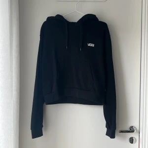 Svart hoodie från Vans med huva - Svart hoodie från Vans i storlek medium. Klassisk modell med huva, snörning och magficka. Liten vit Vans-logga på bröstet. Mjuk och skön, perfekt till chill dagar. Långärmad och i bomullsmix.