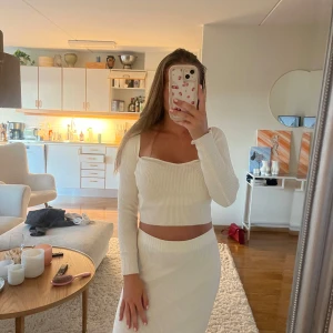 Vit ribbad långkjol med slits - Säljer en snygg vit ribbad tröja tillsammans med en matchande långkjol  med slits i sidan. Kjolen är högmidjad och har en figurnära passform som framhäver siluetten. Materialet på både kjolen och tröjan är mjukt och stretchigt. 