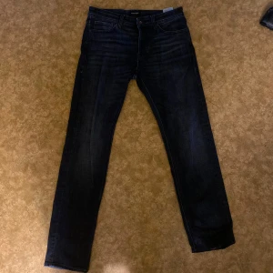 Svarta jeans från Jack & Jones  - Snygga svarta jeans från Jack & Jones i klassisk straight fit. Materialet är slitstarkt denim som sitter skönt hela dagen. Perfekt för dig som gillar stilrena och tidlösa jeans. Skicket är mycket bra och har bara blivit använda ett få tal gånger. 