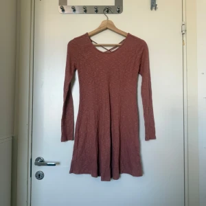 Rosa ribbad kortklänning med snörning - Superfin rosa kortklänning med ribbat tyg och långa ärmar. Klänningen har snygg snörning i ryggen och en lätt utställd kjol. Perfekt för dig som gillar en enkel men ändå cool stil. Färgen är ungefär som sista bilden. Färgen var svår att få på bild. Mycket fint skick, jag hittar inga synliga anmärkningar eller defekter.
