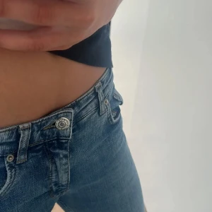 Ljusblå bootcut jeans i storlek 164 - Säljer ett par ljusblå jeans med bootcut passform. Jeansen har låg midja och klassisk femficksdesign. De är tillverkade i mjukt denimtyg och har snygga slitningar för en avslappnad look. Perfekta för dig som gillar en tidlös och trendig stil.