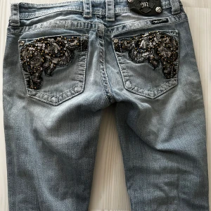 Miss Me ljusblå jeans med paljettdetaljer 400kr om du kan mötas!!! - Snygga ljusblå jeans från Miss Me med unika paljettdetaljer och broderier på bakfickorna. Klassisk femficksmodell med silverfärgade knappar och logga. Jeansen har en normal passform och är tillverkade i mjukt denimtyg.